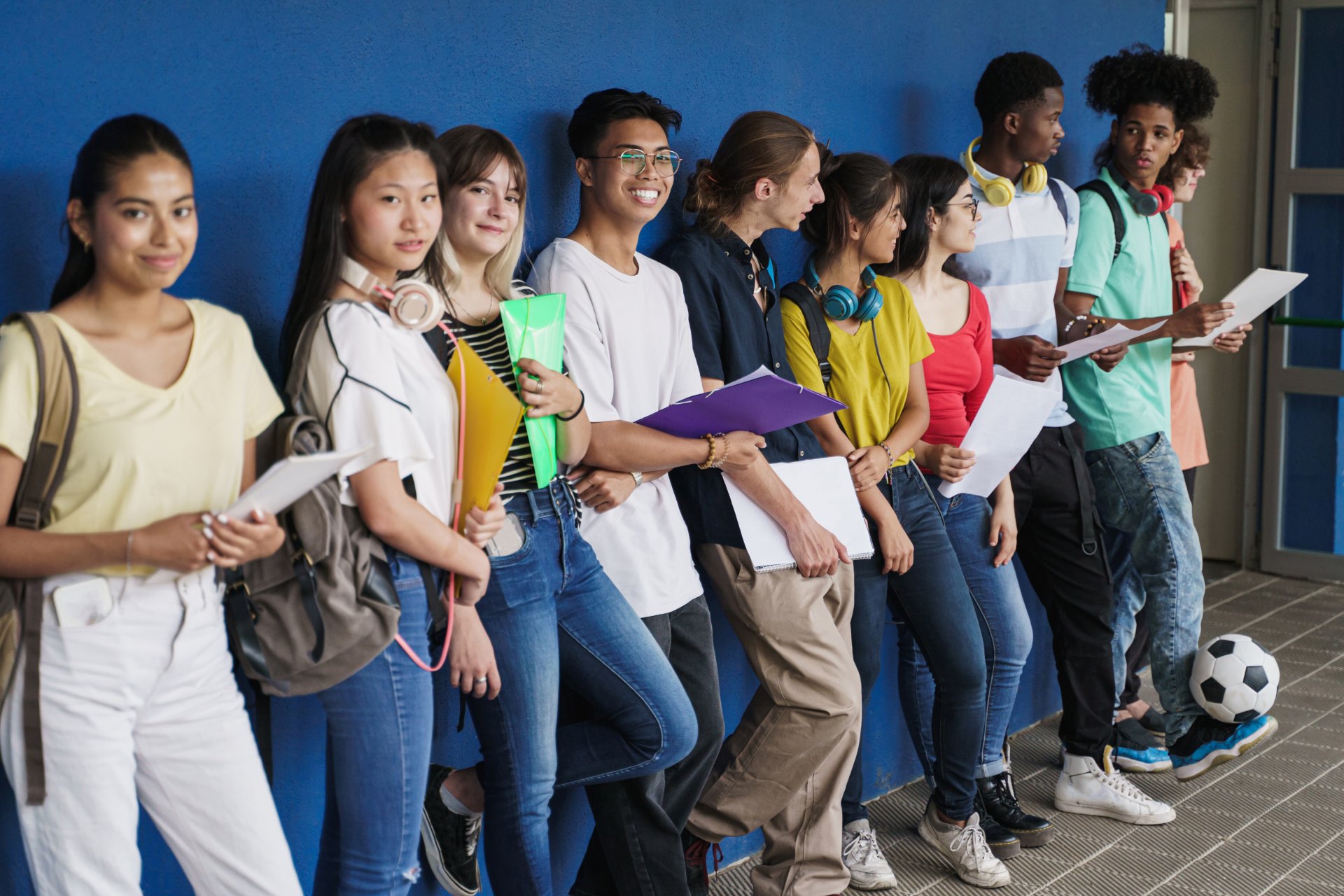 Group of multiracial teenager friends standing over blue wall. Happy Multi ethnic students in Secondary School. Focus on Center Chinese Girl Group of multiracial teenager friends standing over blue wall. Happy Multi ethnic students in Secondary School. Focus on Center Chinese Girl